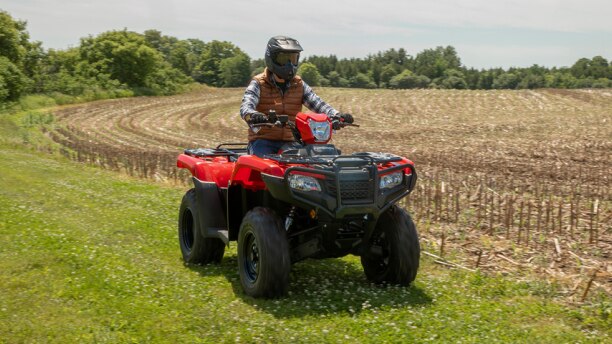 A rider on a Honda Foreman driving beside a farm