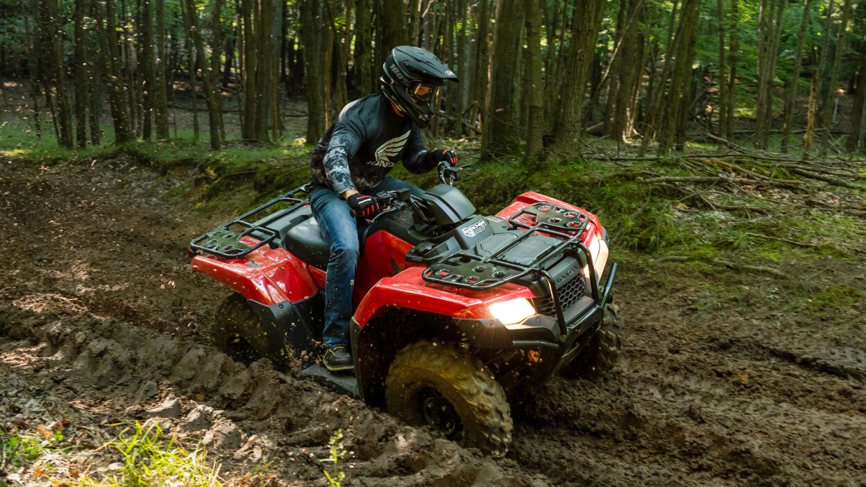 Un conducteur au volant d'un 4x4 tourne à droite sur un chemin de terre. Paysage boisé en arrière-plan.