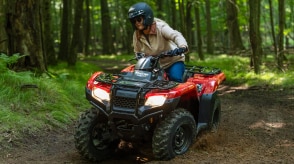 Un conducteur au volant d'un 4x4 tourne à gauche sur un chemin de terre. Paysage boisé en arrière-plan.