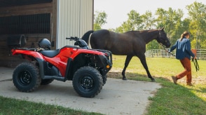 Un éleveur immobile devant une grange. Une femme fait sortir un cheval de la grange en arrière-plan.