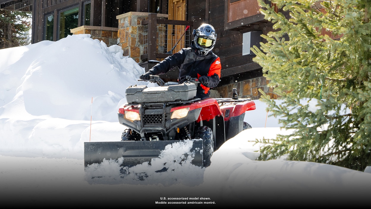 Person operating an ATV equipped with a snowplow in snow