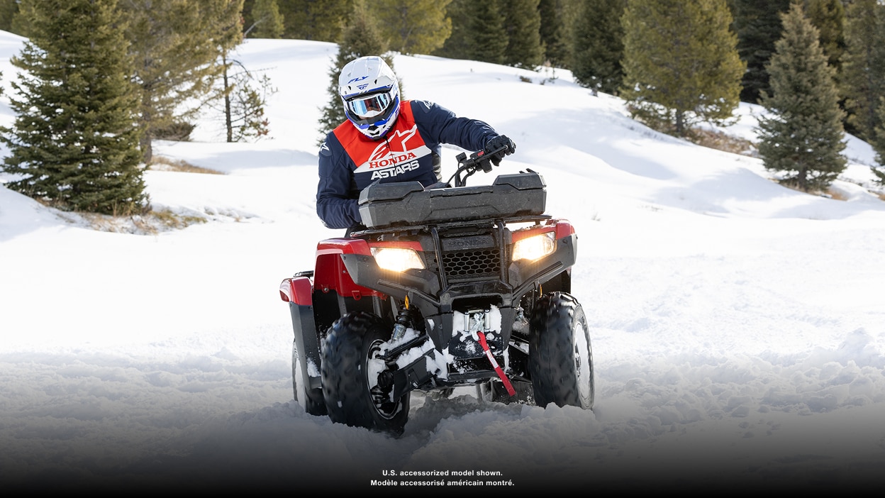 Person riding an ATV with a front cargo box through snow