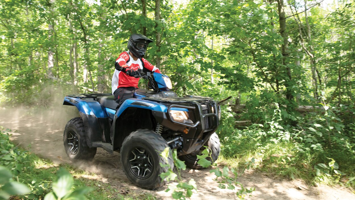 A rider on a partially sunny trail in the forest on a Honda Rubicon