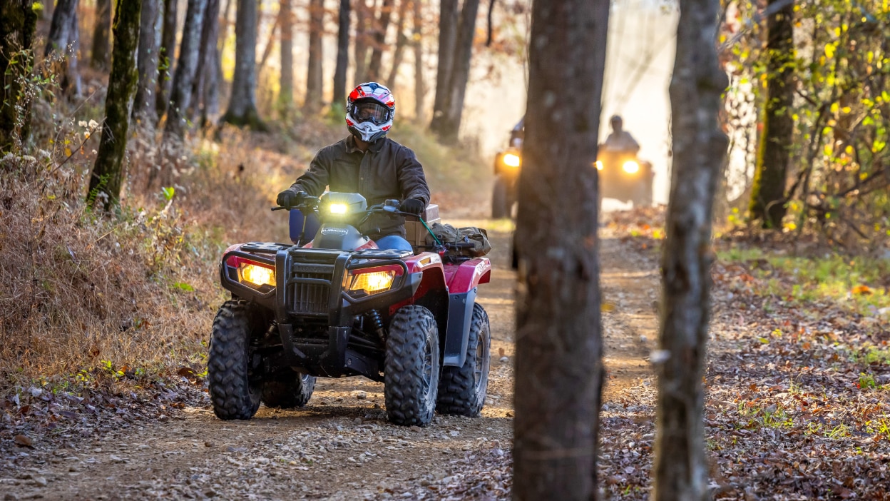 Un pilote sur un sentier forestier sur une Honda Rubicon 700. 