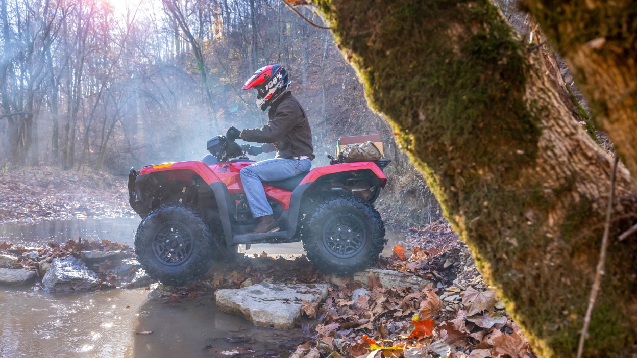 Un pilote sur le point d'entrer dans une grande flaque d'eau dans une zone boisée sur une Honda Rubicon 700.