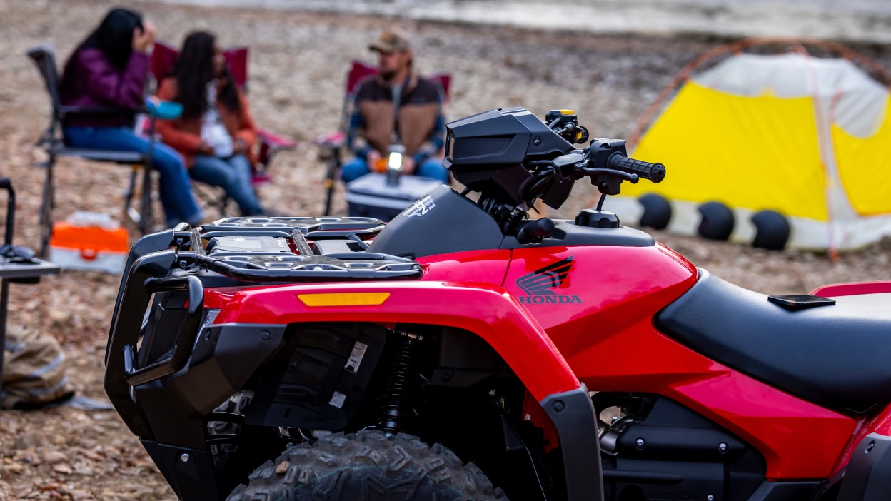 Un camping en arrière-plan avec une Honda Rubicon garée au premier plan. 