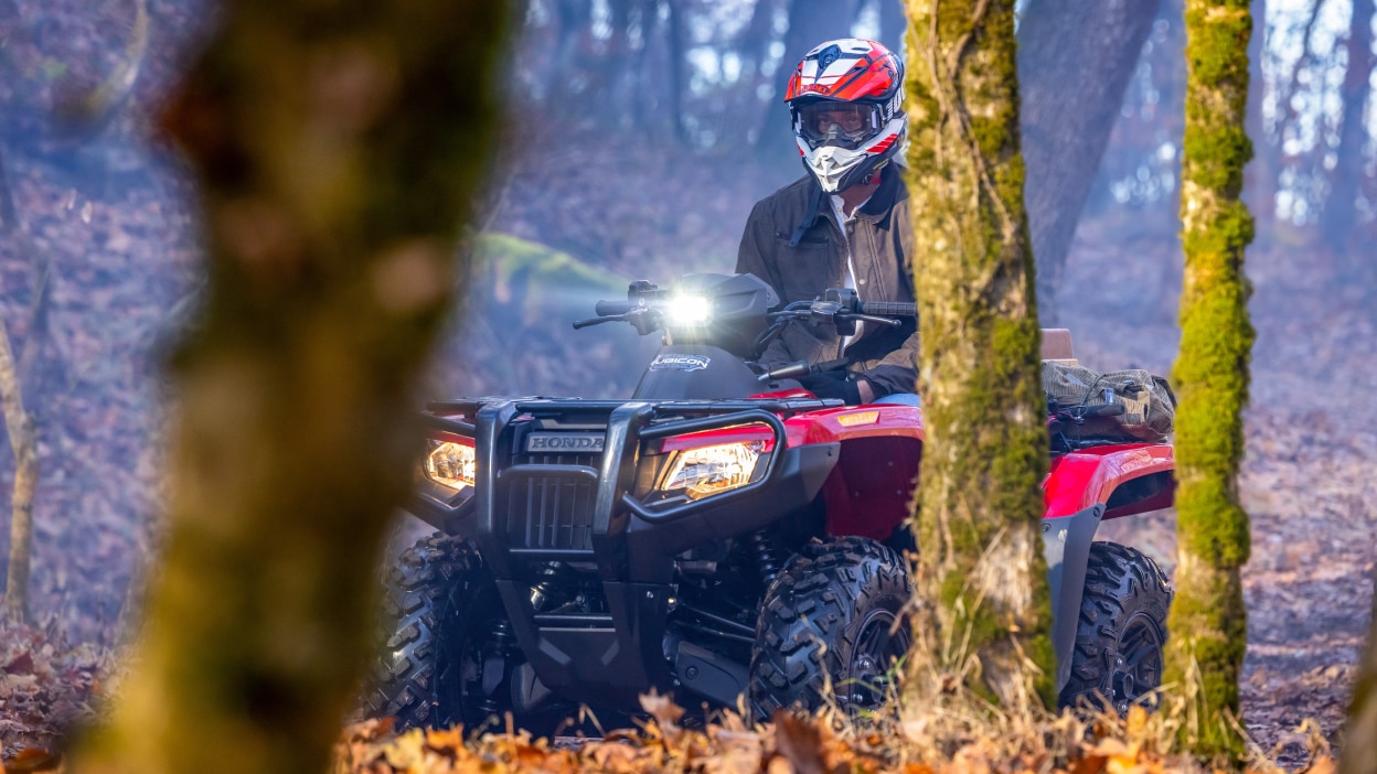 Un pilote derrière quelques arbres au premier plan sur une Honda Rubicon 700 