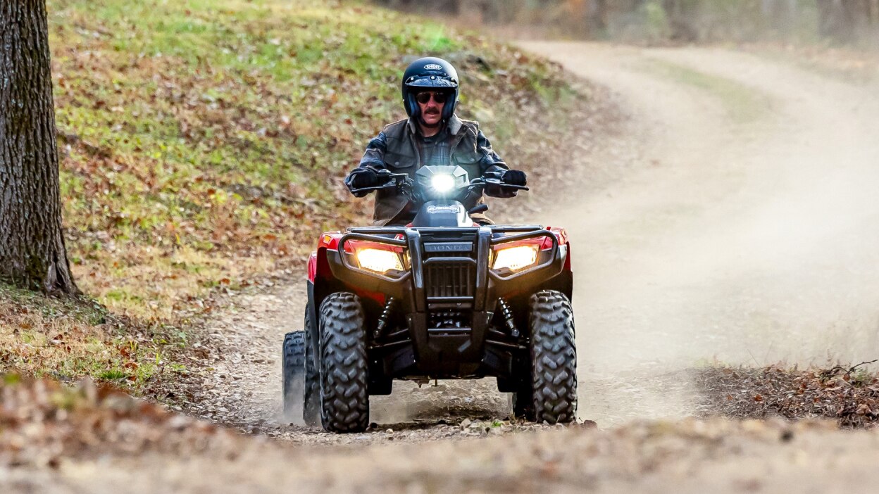 Un homme conduisant un Rubicon 700 sur un sentier en automne avec les phares allumés. 