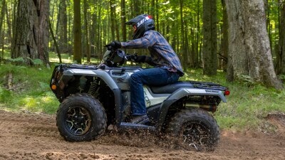 Un conducteur au volant d'un Rubicon gris tourne à gauche sur une route très boueuse. Paysage boisé en arrière-plan.