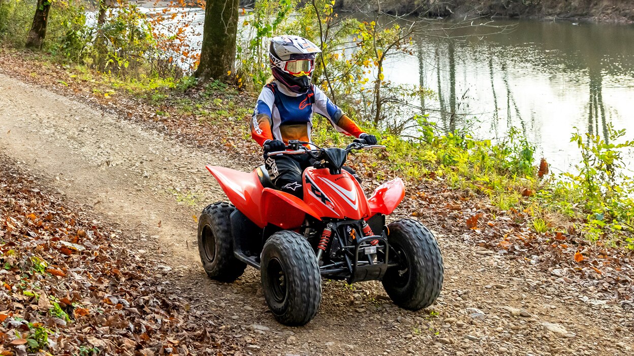 Jeune pilote de quad en forêt, sur un chemin de terre. Rivière en arrière-plan.
