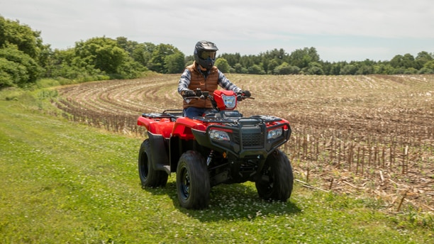 Un cavalier sur une Honda VTT à côté d'un champ d'agriculteur