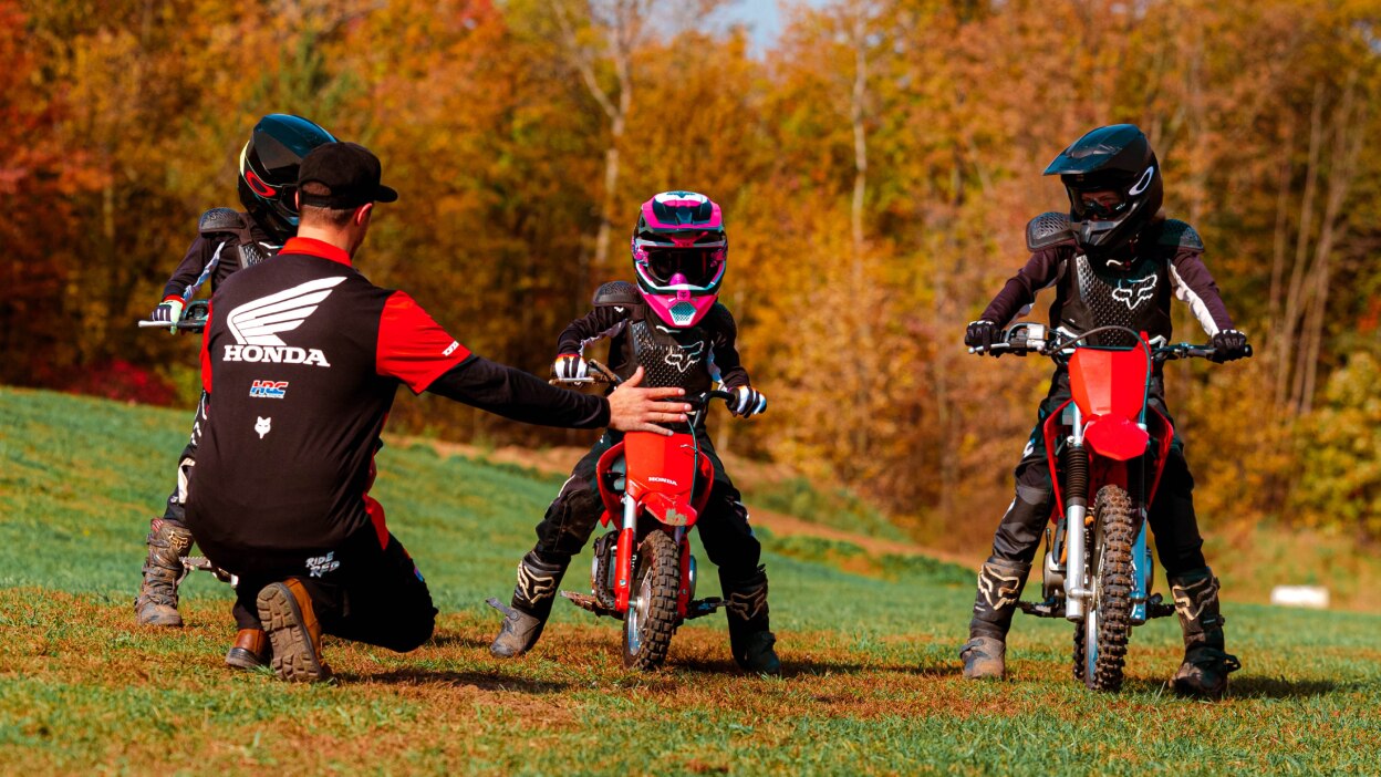 An instructor kneeling to help three Junior Red Riders 
