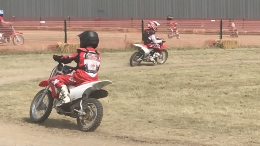 Junior Red Riders on a dirt track, play icon showing users there is a video 