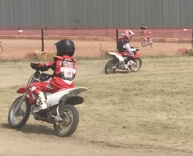 Junior Red Riders on a dirt track, play icon showing users there is a video 