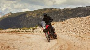 A rider on an Africa Twin in full riding gear on black sand in the mountains