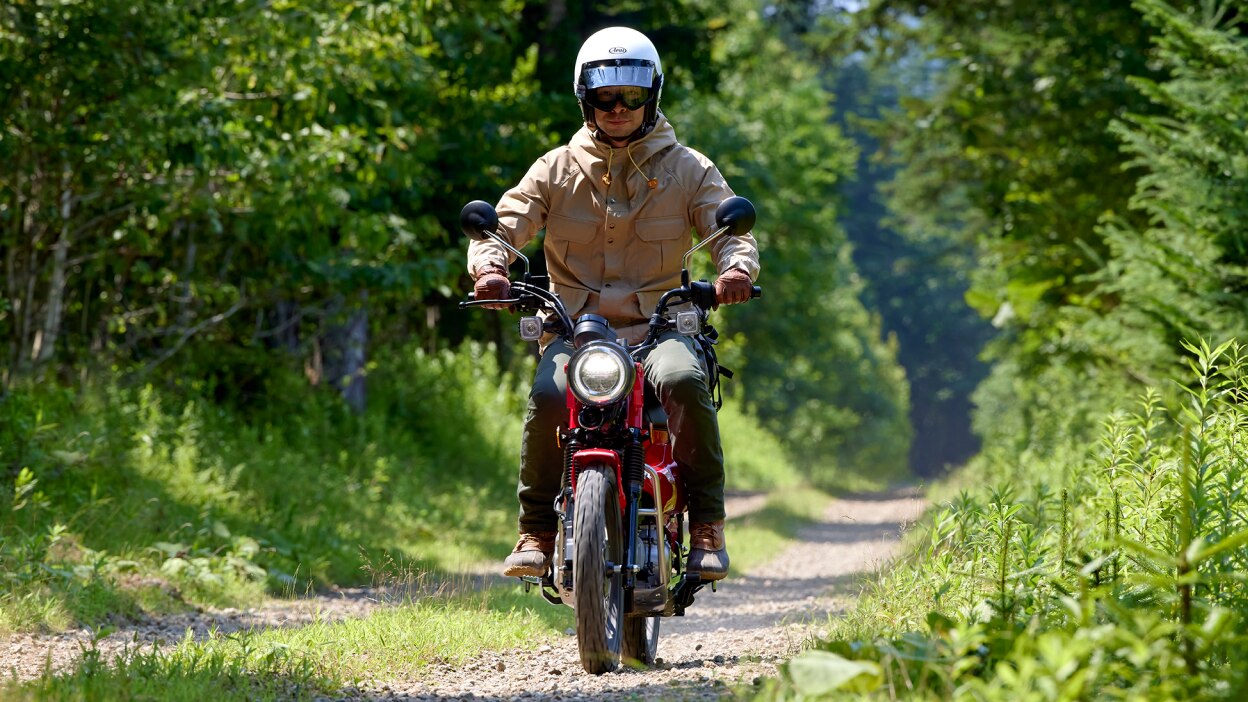 Cavalier avec veste beige sur vélo rouge traversant la forêt sur une route en pierre