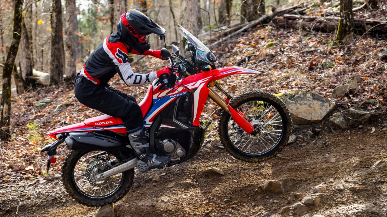 A rider on a Honda Dual Sport dirt bike riding on a rugged trail in the fall