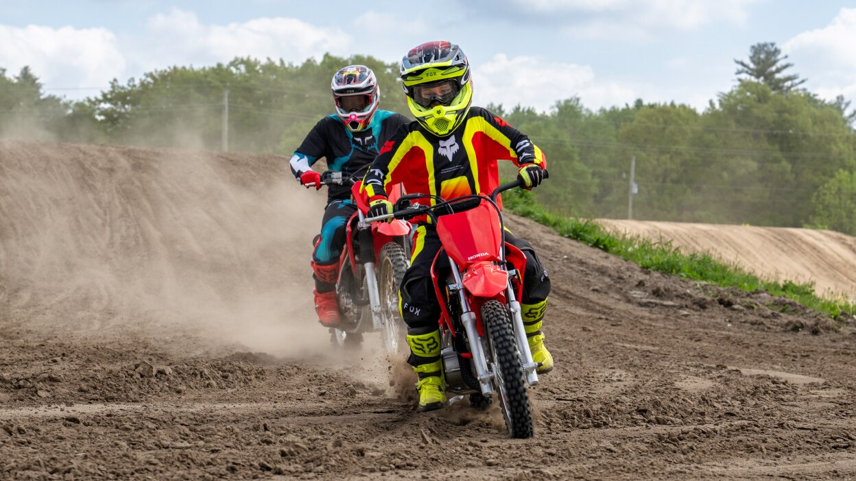Young rider in front of adult rider on dirt track.