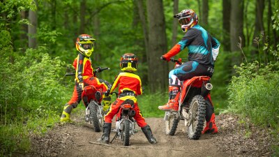 One young rider and adult rider looking back at another young rider in forest landscape.