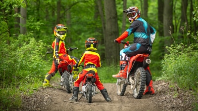 One young rider and adult rider looking back at another young rider in forest landscape.