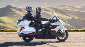 Deux coureurs sur un vélo blanc vont à droite. Green Hills en arrière-plan.