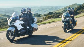 Deux coureurs sur vélo blanc devant deux coureurs sur vélo vert sur route. Collines en arrière-plan.