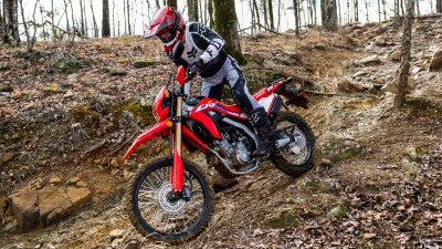 A side angle view of a person riding the Honda CRF300L in the forest