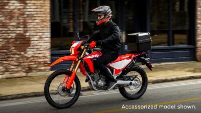 A side angle view of a person riding the Honda CRF300L on a city street, accessorized model shown