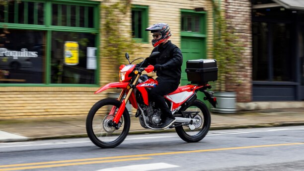 A side angle view of a person on a CRF300L in the city, accesorized model shown