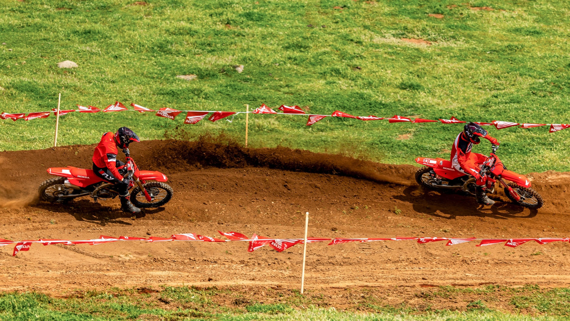 Two riders on dirt track, facing right. one on each side of image.