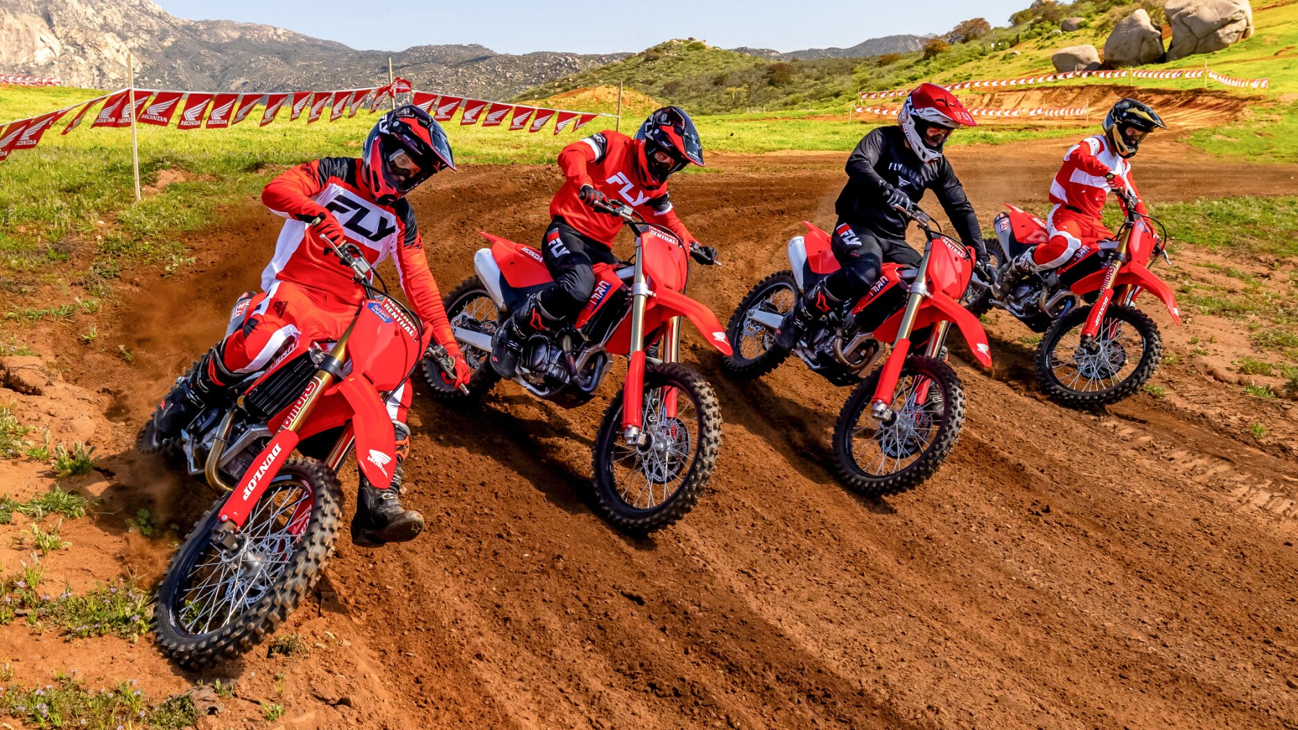 Four riders turning left on dirt track. Front facing.