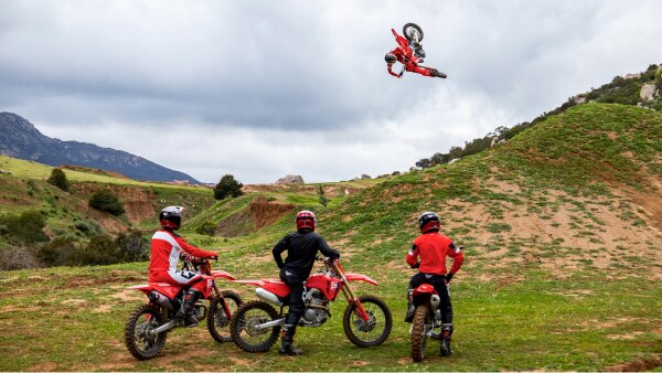 Three riders at bottom of hill watching one rider mid air. Lifestyle.