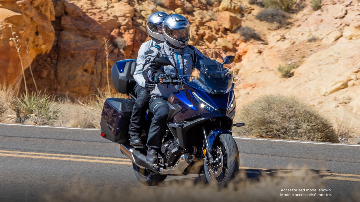 Rider and passenger facing right on NT1100. Desert landscape in background.