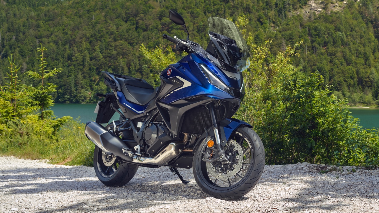 NT1100 stationary on pebble road. Green forest, bushes and lake in background.