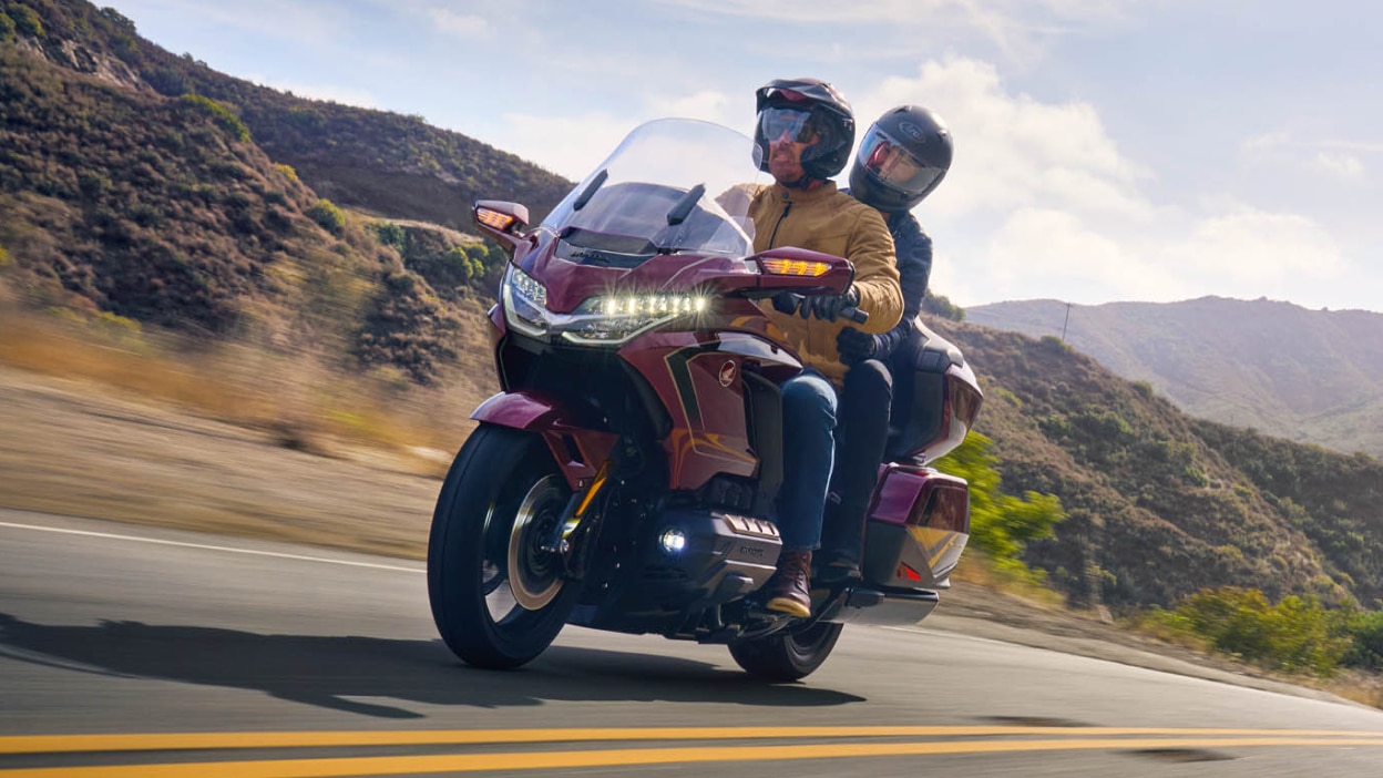 Pilote et passager du Red Gold Wing Tour en allant à gauche sur la route. Montagnes en arrière-plan.