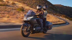Rider and passenger on Gold Wing making left turn on bend in road. Mountain landscape.