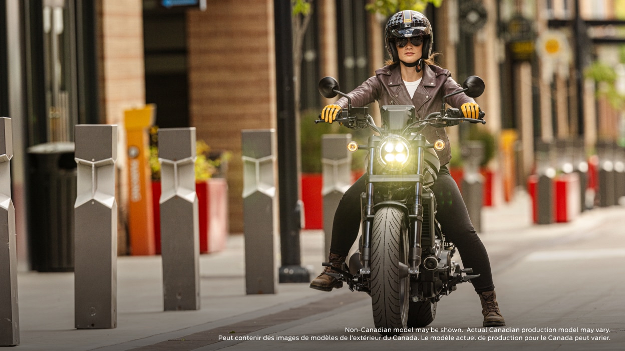 Front facing of rider on bike on road with headlight on. Side wall with pillars to the left. Non-Canadian model(s) may be shown. Actual Canadian production model(s) may vary.