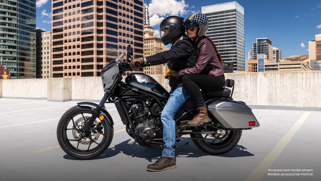 Rider and passenger stationary in car part. Skyline of building and blue sky in background. Accessorized model shown.