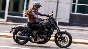 Rider on Black Rebel 1100 going right on road. Grey building with large windows in background.
