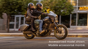 Rider and passenger going right on Rebel 1100 Touring on road. Building, side walk and trees in background. Accessorized model shown.