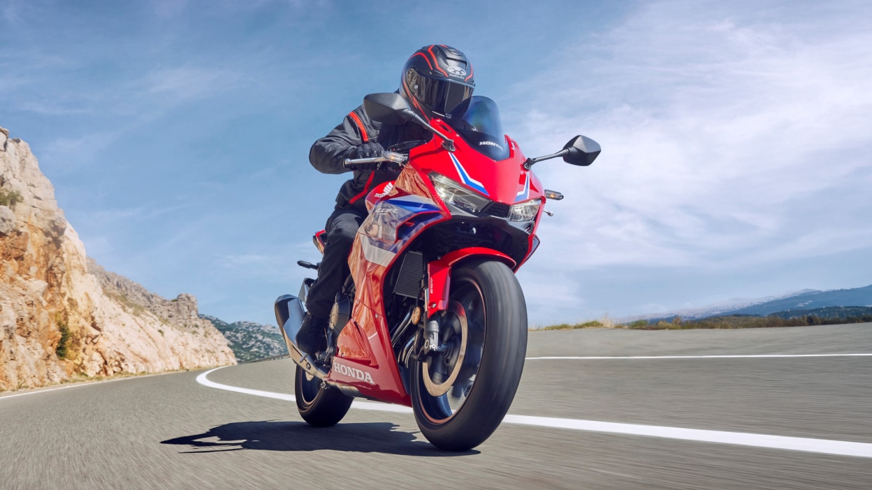Petite image d'une personne conduisant une moto sport rouge près de la côte.