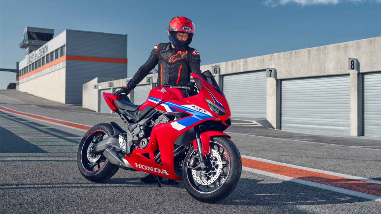 Petite image d'une personne conduisant une moto sport rouge le long d'une route côtière.