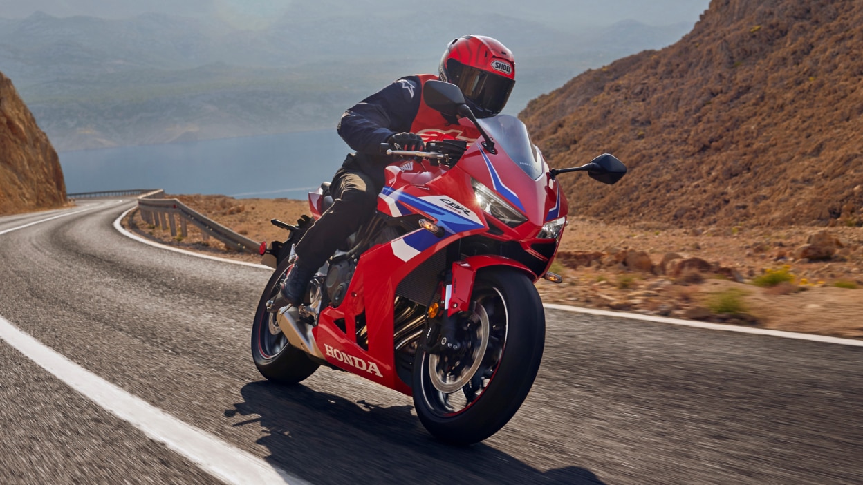 Pilote chevauchant le Grand Prix Red Fireblade sur piste. Face avant. Suivi en arrière-plan. Buissons verts derrière l'arrière-plan de la piste.