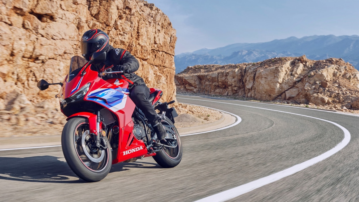Pilote chevauchant le Grand Prix Red Fireblade sur piste. Face avant. Suivi en arrière-plan. Buissons verts derrière l'arrière-plan de la piste.