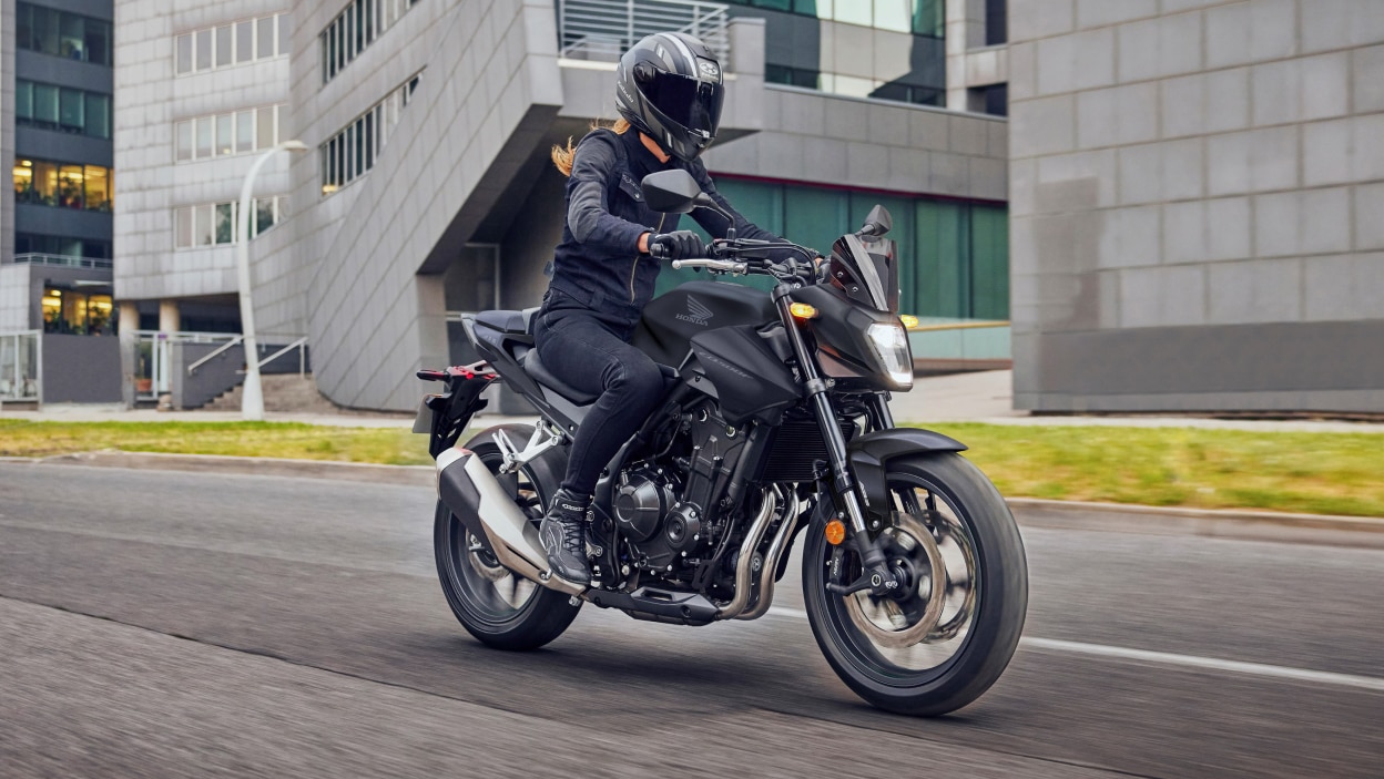 Cavalier aux cheveux longs conduisant sur route. Bâtiment gris avec de grandes fenêtres en verre en arrière-plan.