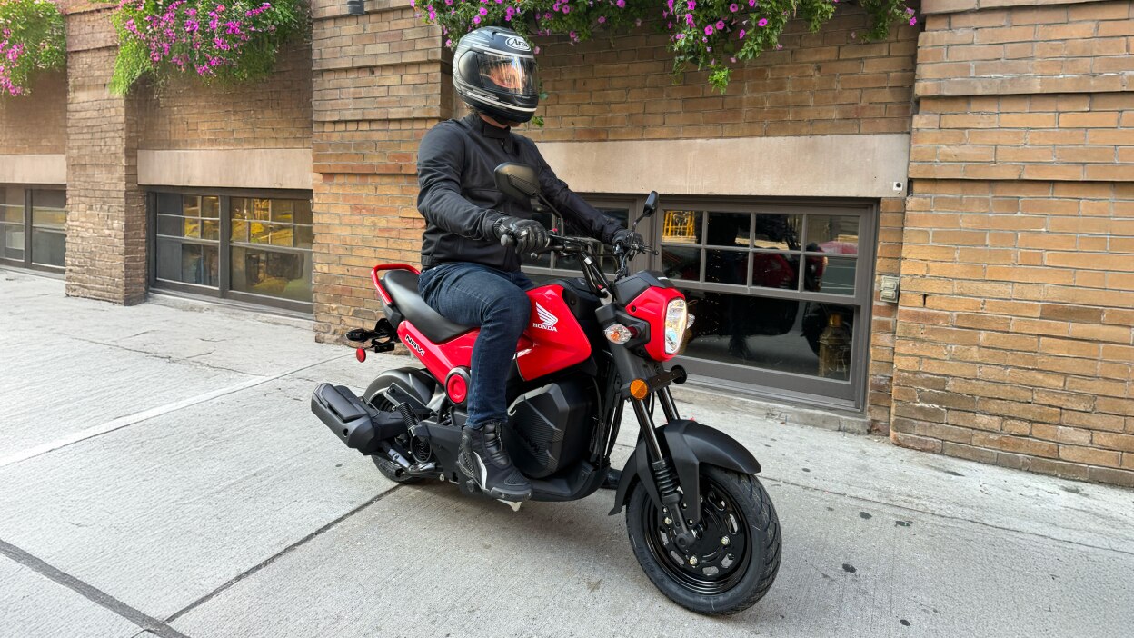 Personne à côté de Navi avec les mains sur les poignées. Bâtiment en brique en arrière-plan.