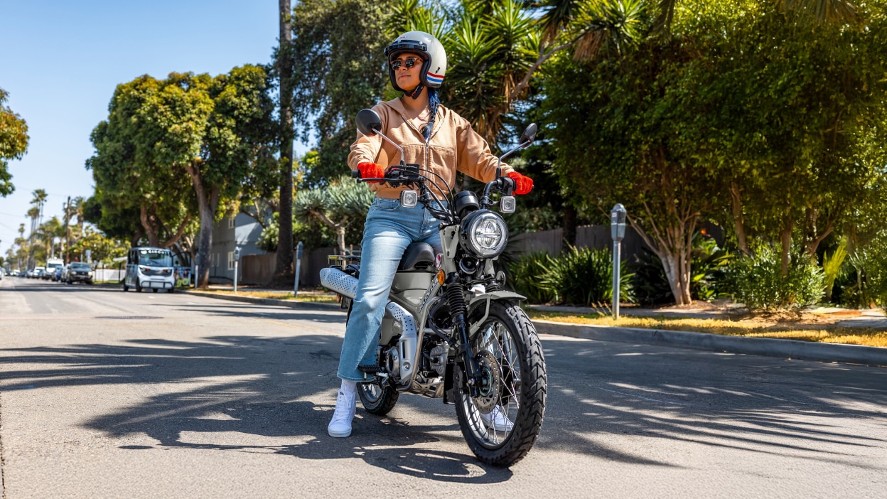 Person on Grey bike, stationary in street. Trees and cars in background.