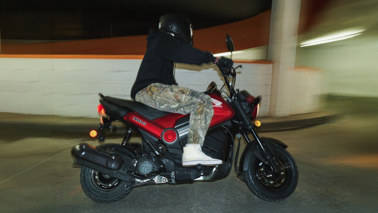 Un motard sur un Navi tourne à gauche sur la route. Mur blanc en arrière-plan.