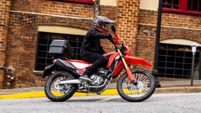 Pilote sur CRF300L allant vers la droite. Bâtiment en briques en arrière-plan.