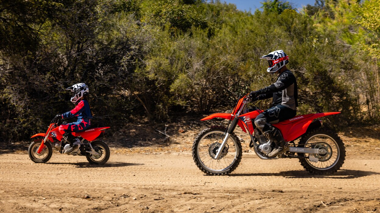 One young rider in front of adult rider, going left. Left angle.